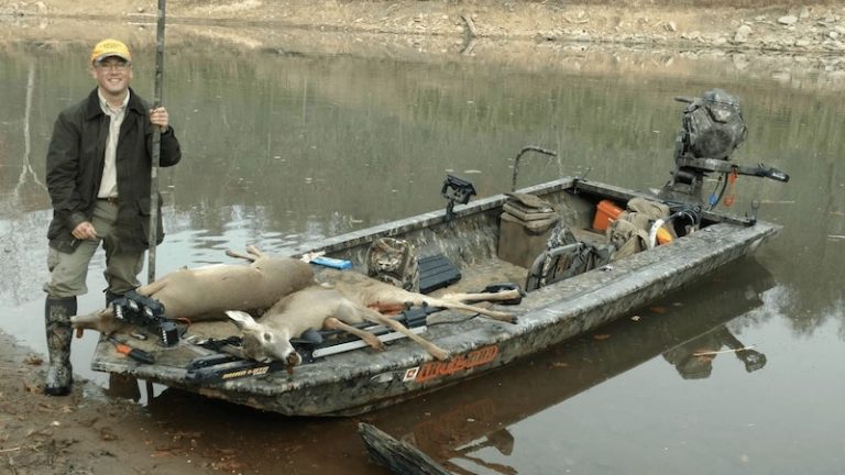 Hunter with a deer in a camo mud boat at the water's edge