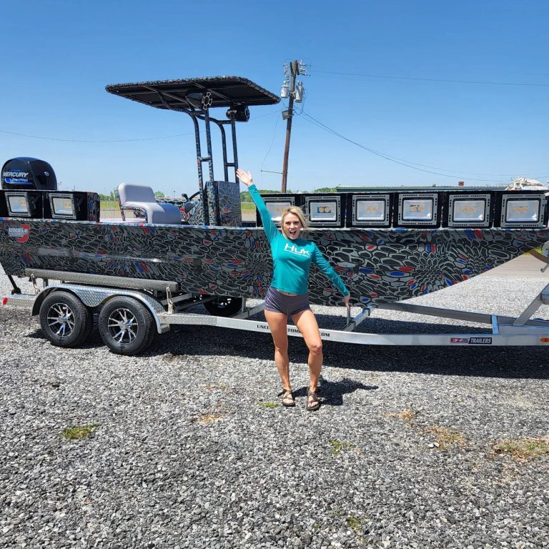 Woman beside a camo bowfishing boat with a T-top on its trailer