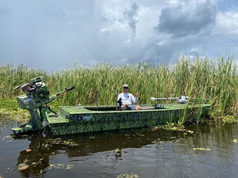 Green camo mud boat with a surface drive motor in front of tall marsh grass