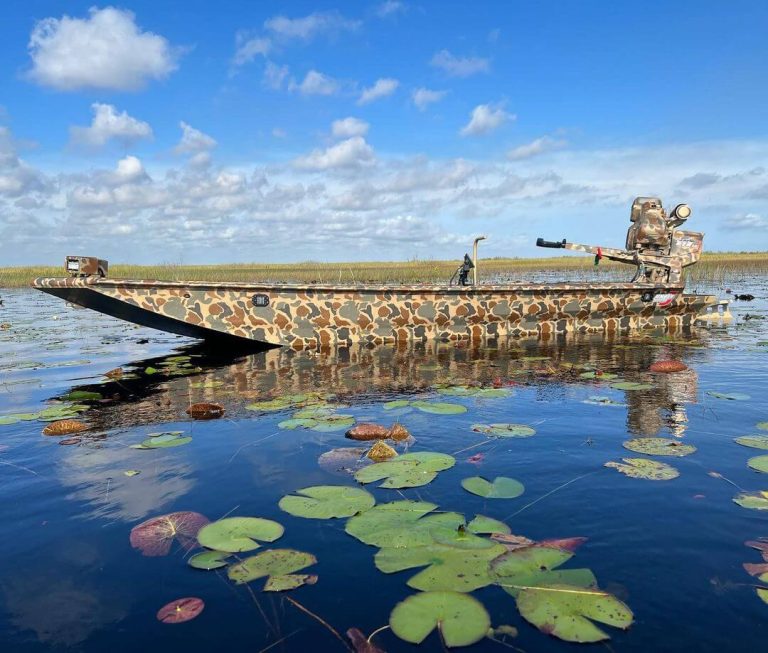 Camo mud boat with a surface drive motor on calm water among lily pads