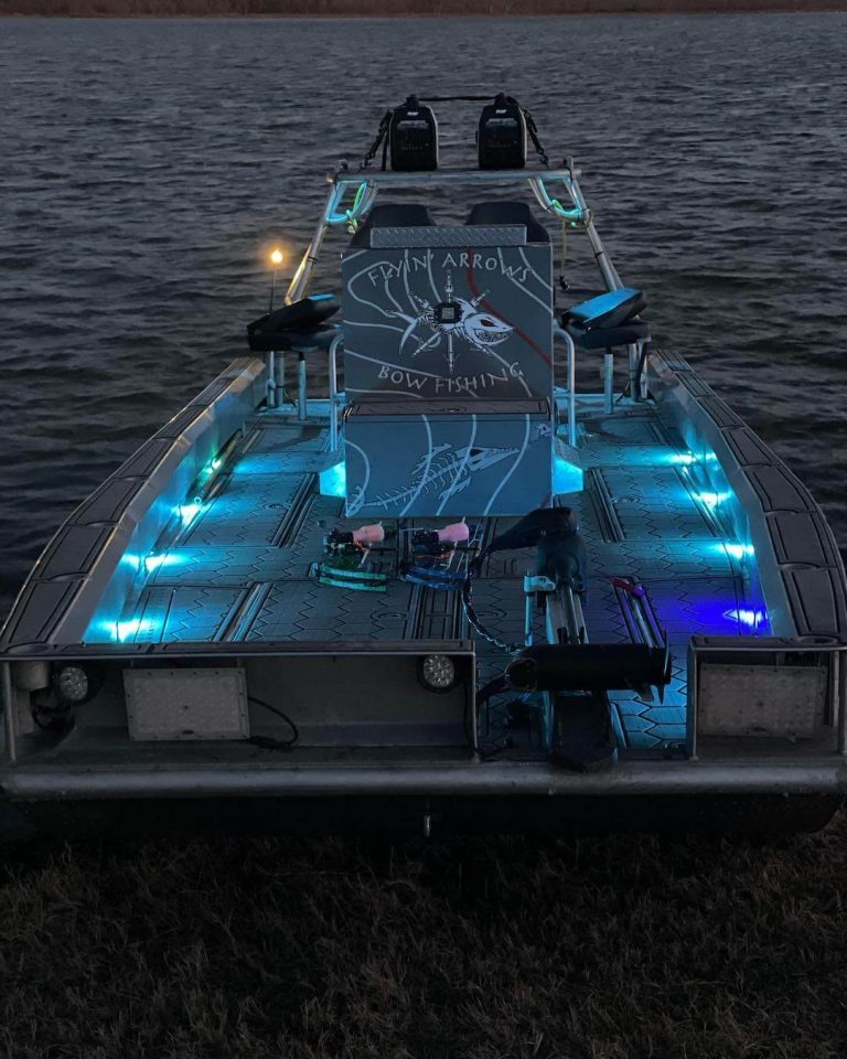 Flyin' Arrows Bowfishing boat lit with blue deck lights at dusk