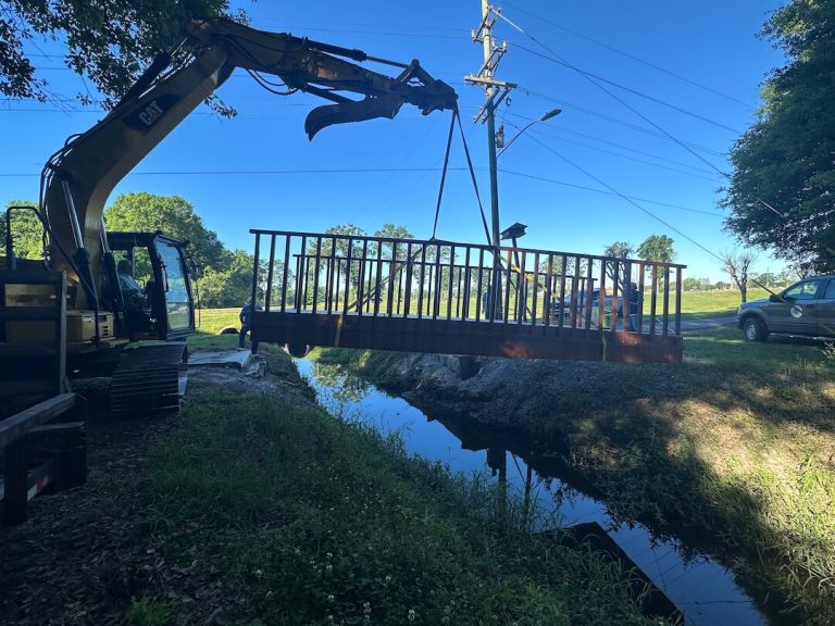Excavator lowering an aluminum walking bridge over a canal