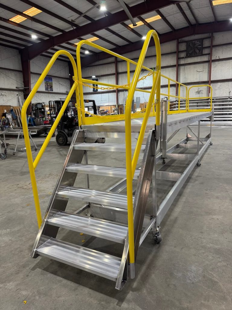 Aluminum stairs with yellow handrails leading up to a work platform