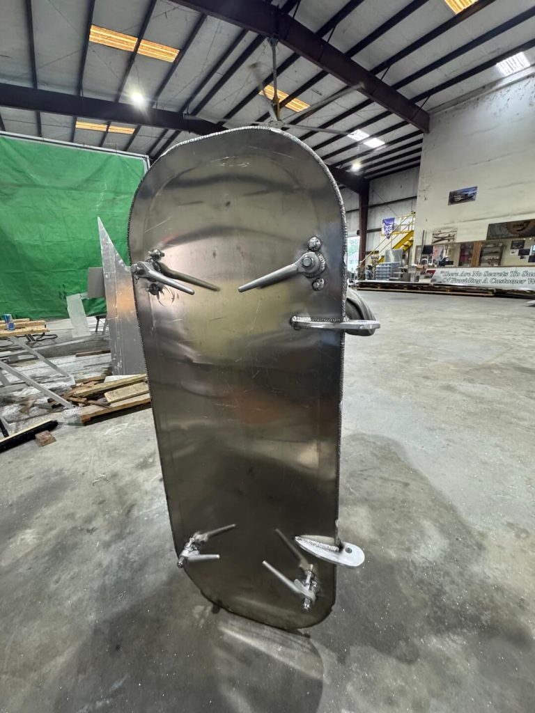 Rounded aluminum hatch door with lever latches, standing in the shop