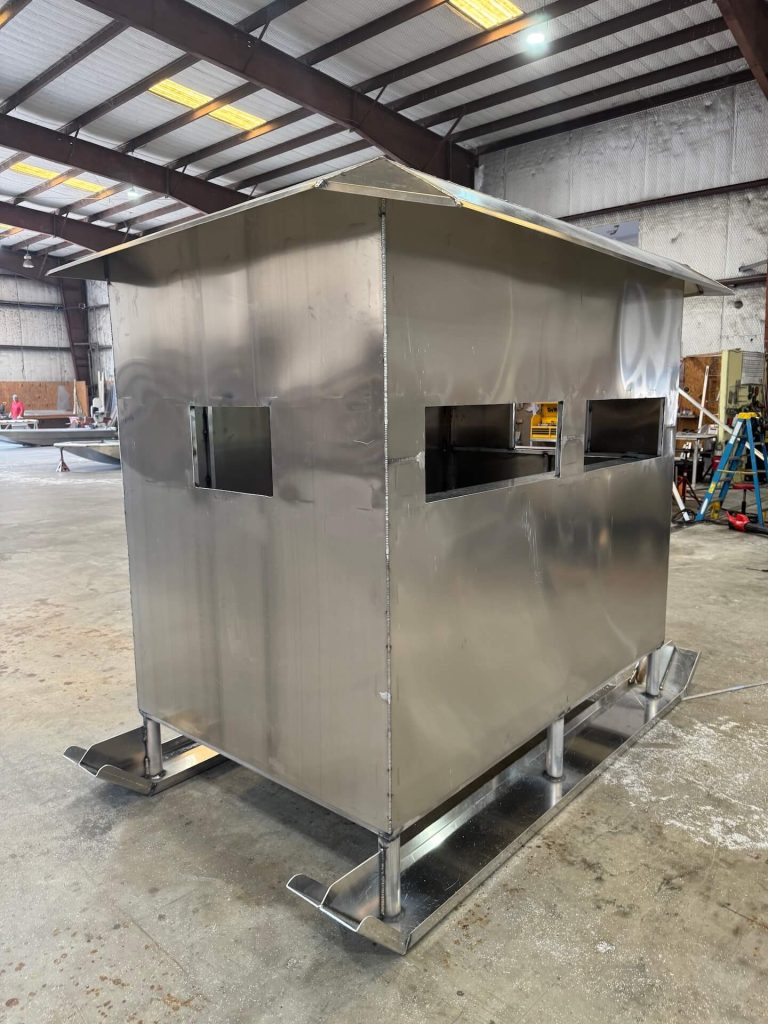 Aluminum enclosure with a sloped roof and window openings, on skid runners